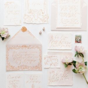 Flat lay of elegant calligraphy invitation suite with floral accents. Perfect for weddings and events.