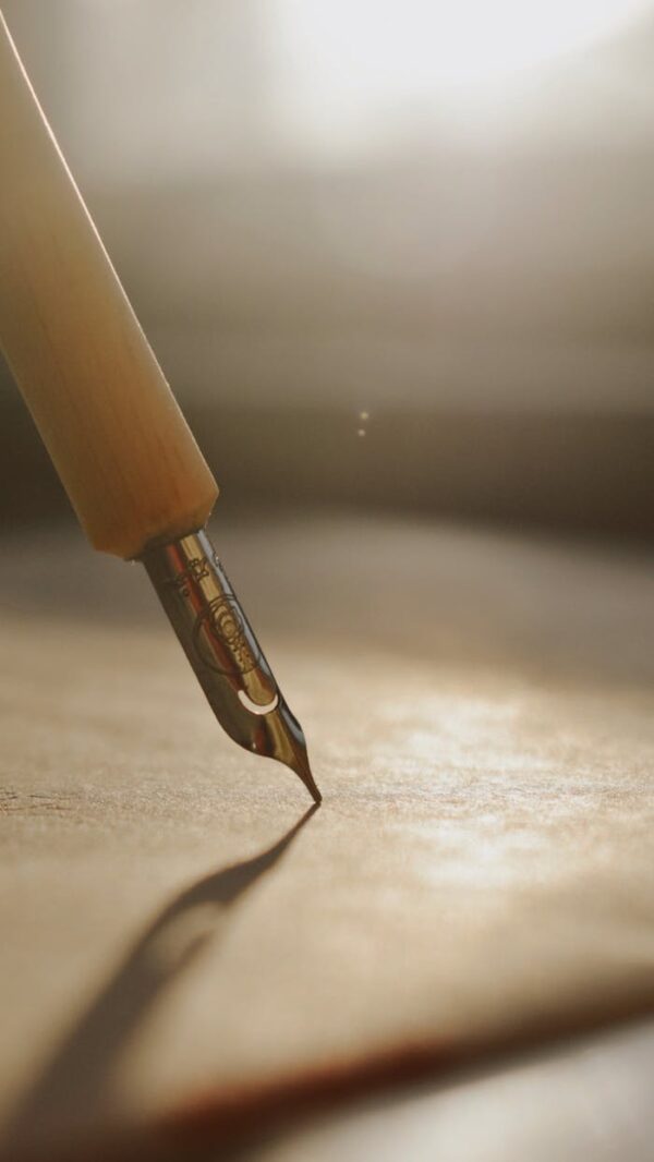 Close-up of a fountain pen tip casting shadow on paper, bathed in warm sunlight.